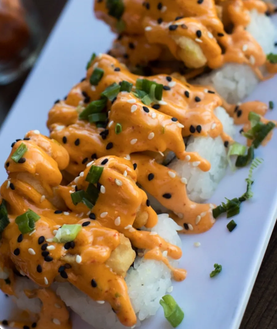 Rollos cubiertos de salsa cremosa, ajonjolí negro y cebollín.